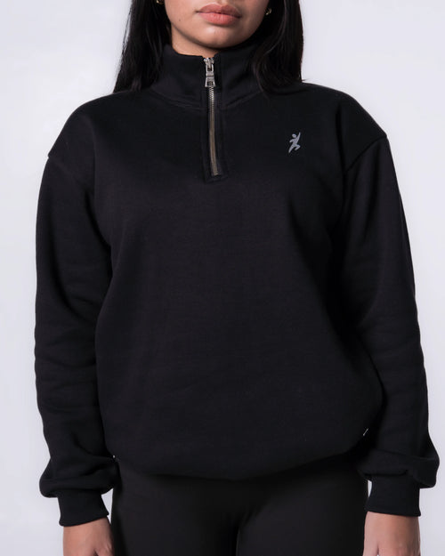Person wearing a Black quarter-zip sweatshirt with a logo on a white background
#color_black
