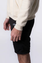 Person wearing a beige hoodie and Black shorts with a brand logo on a white background
#color_black