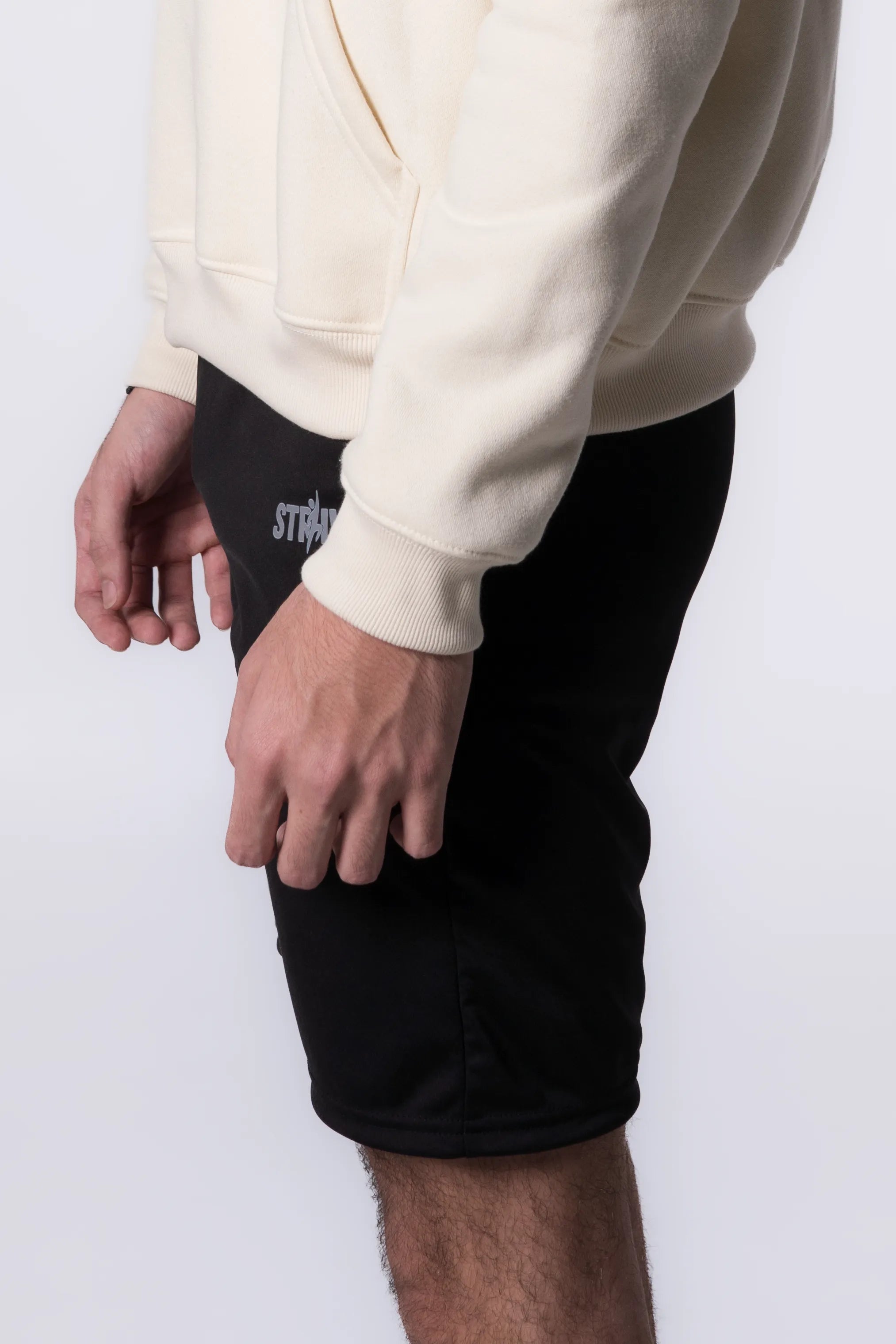 Person wearing a beige hoodie and Black shorts with a brand logo on a white background
#color_black
