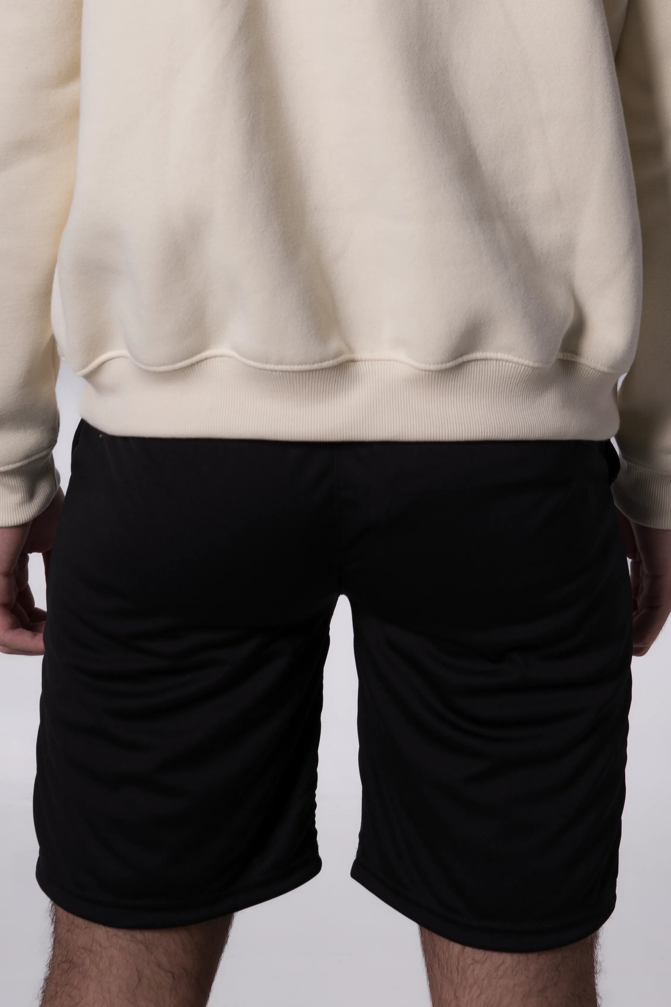 Person wearing a beige sweatshirt and Black shorts on a plain background
#color_black